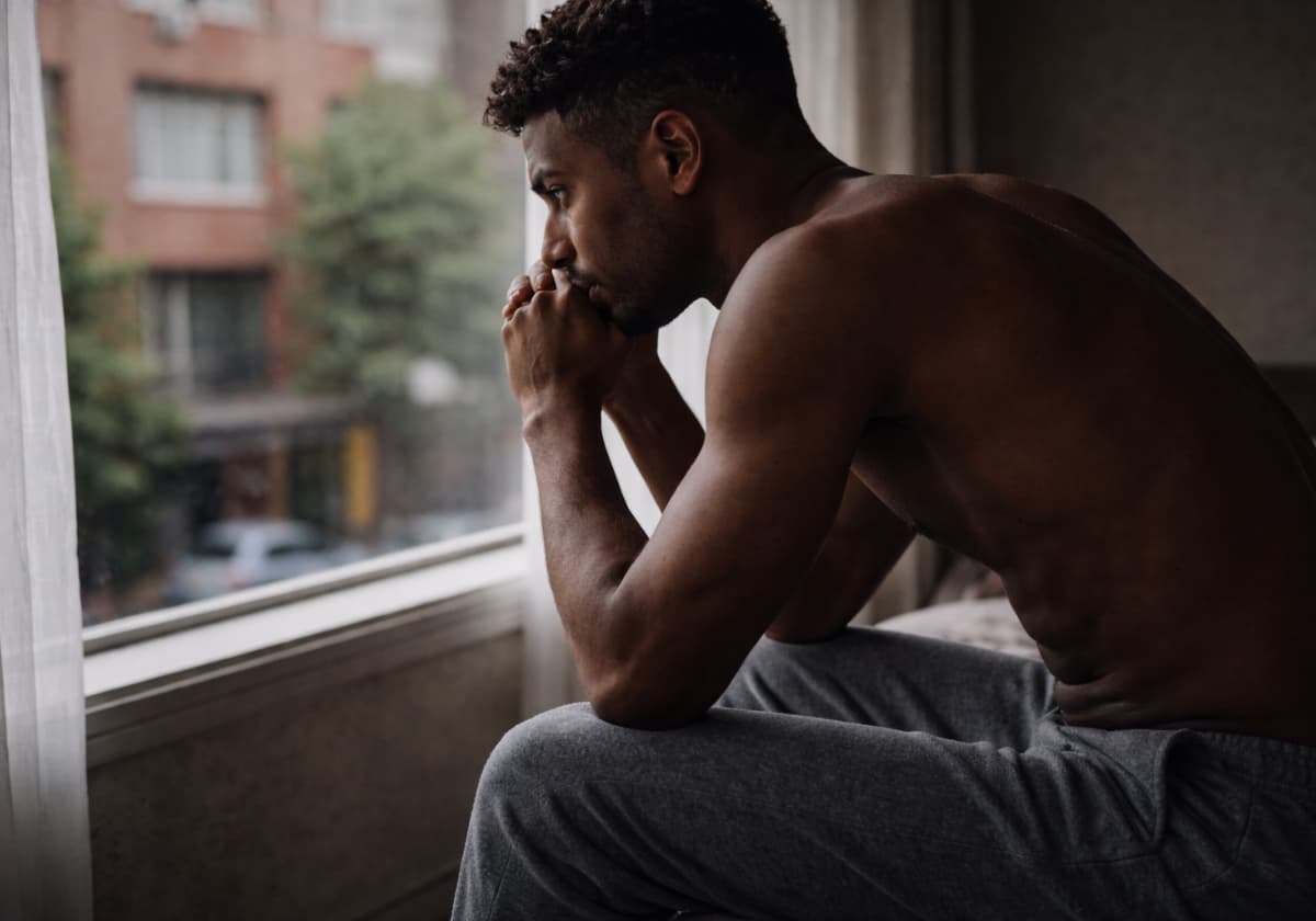 A gay man looking at his reflection in a window at dusk, expression unreadable